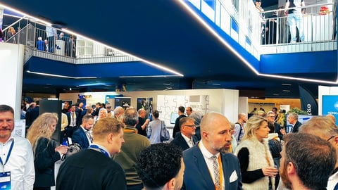 Crowd of people at an indoor conference or trade show venue with modern blue and white architecture and lighting